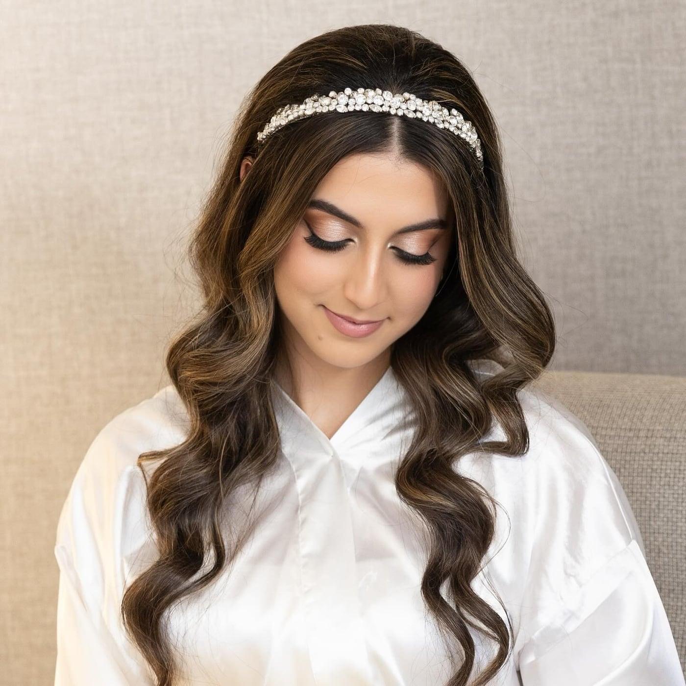 Bride in a satin robe with soft glam makeup, long waves, and a pearl headband