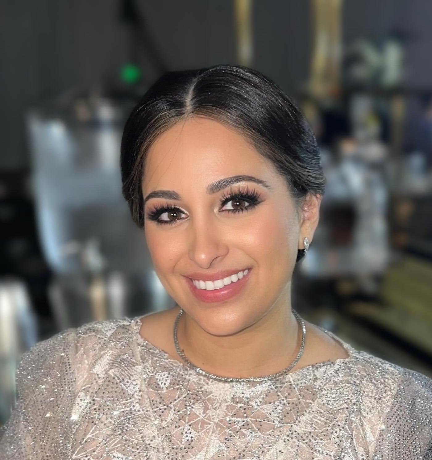 Smiling client with glam makeup, lashes, and sleek hair in a sequin top