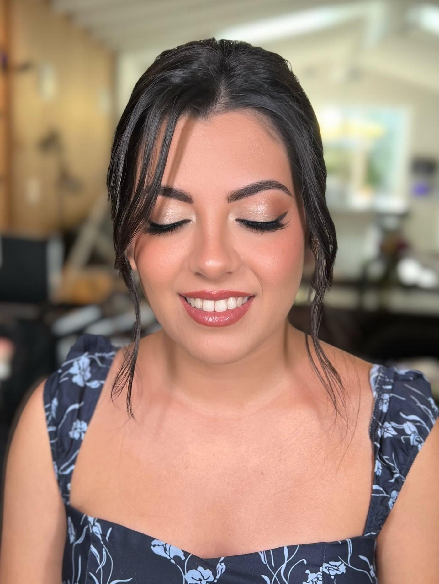 Smiling client with soft glam makeup, winged liner, and a loose updo