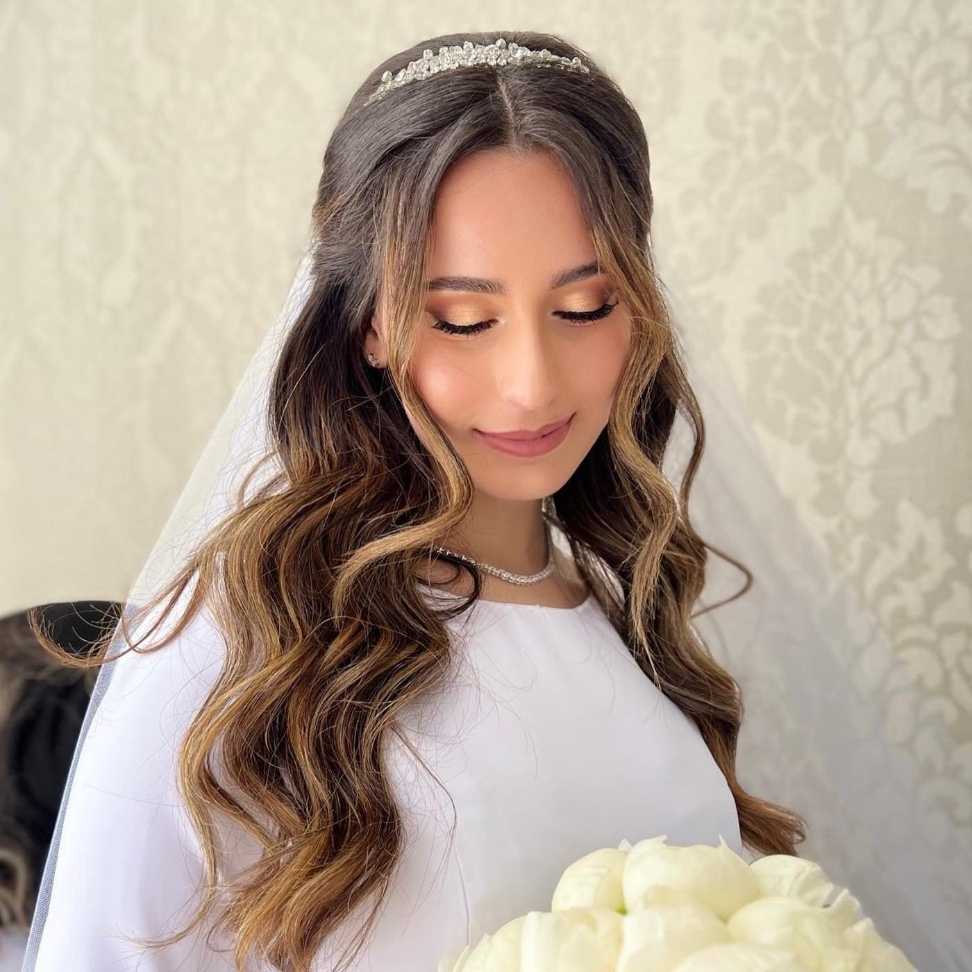 Bride with soft glam makeup, long waves, a veil, and white roses