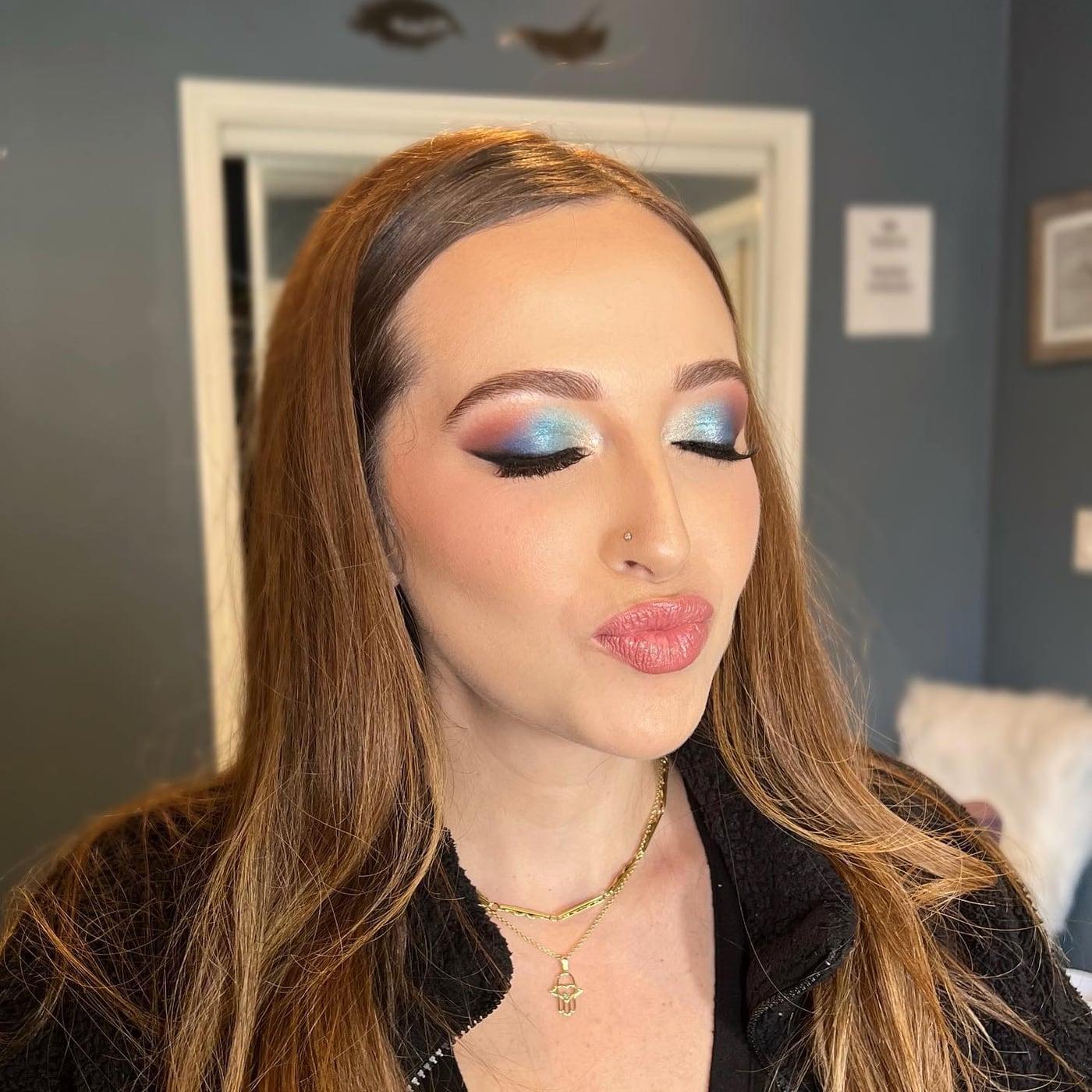 Client with blue and pink glitter eyeshadow, lashes, and a glossy pink lip