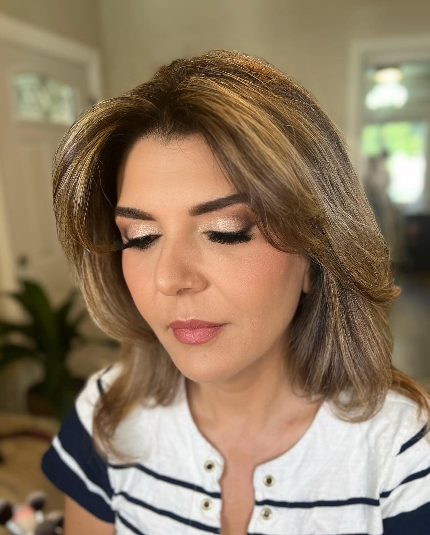 Client with bronze soft glam eyes, lashes, and a mauve lip, looking down