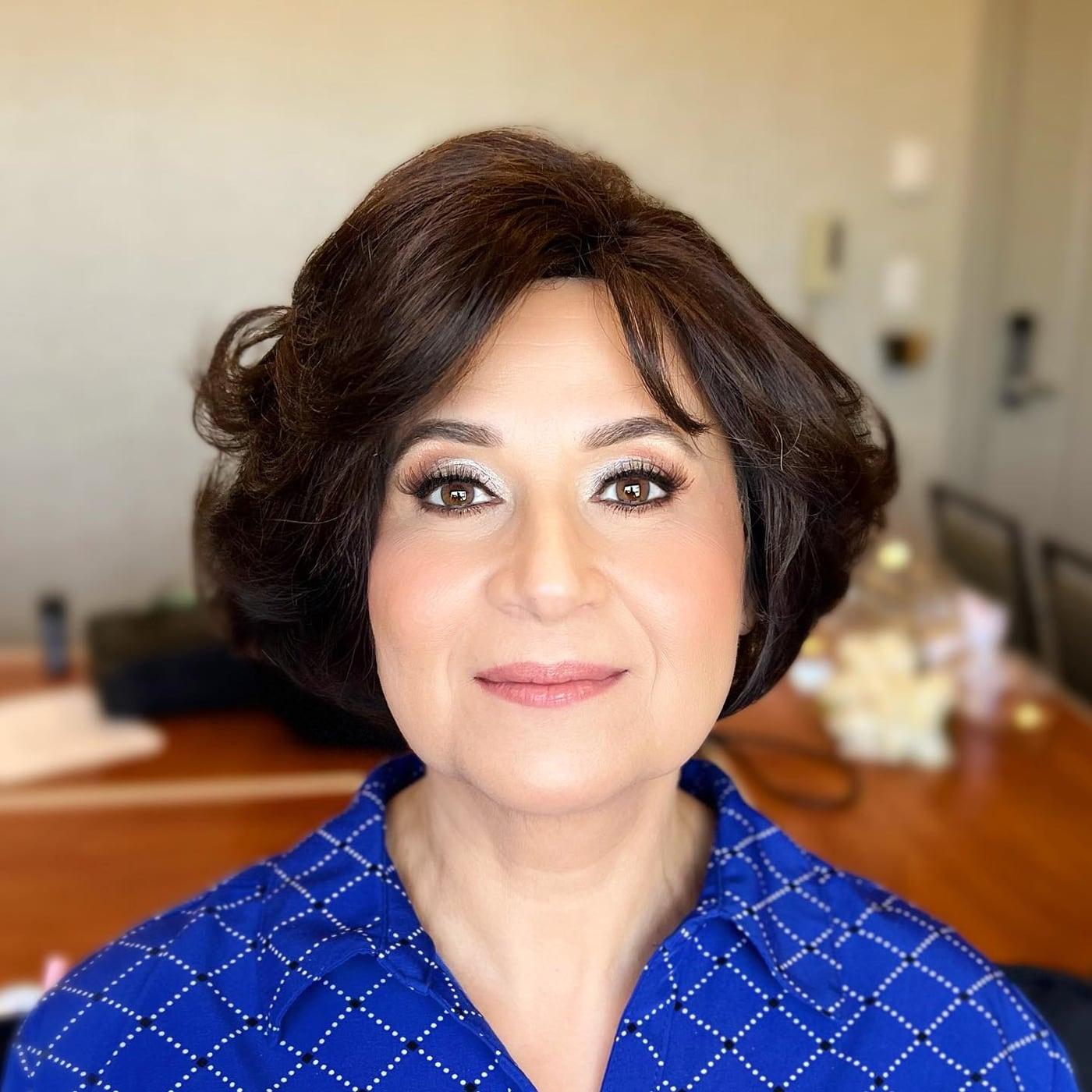 Mature client with soft glam makeup, defined brows, and a rose lip in a blue top